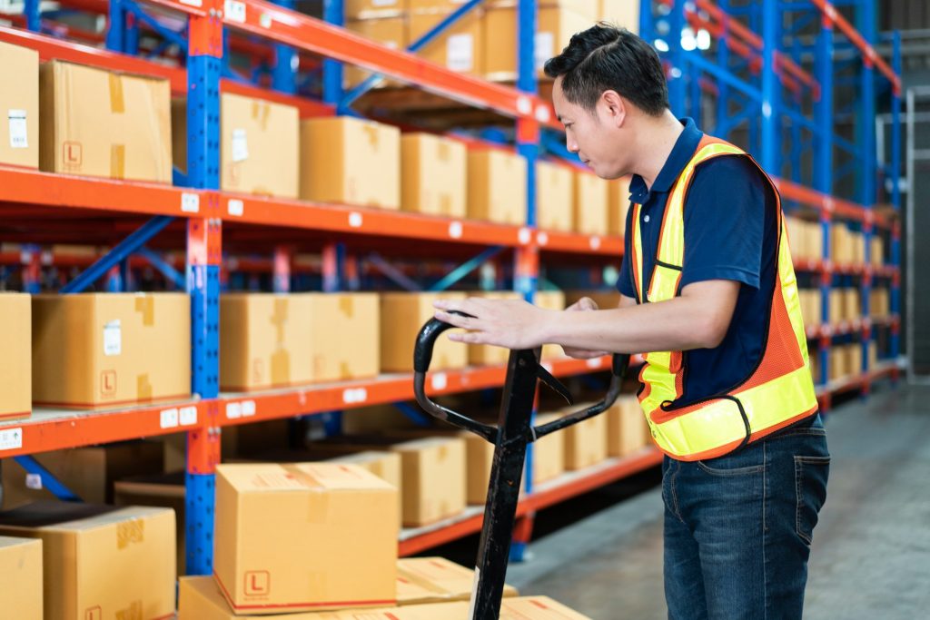 Asian male worker pushing trolley with boxes to the shelves at the warehouse